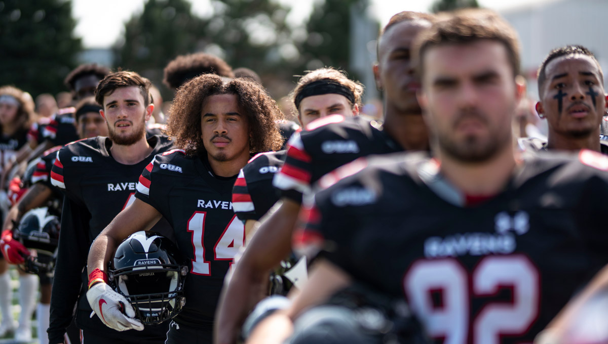 The 2019 Carleton Ravens stand ready for a game to begin while holding their helmets.