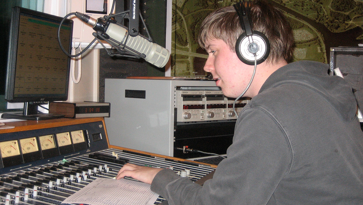 Photo of Nicholas Osborne with headphones on, sitting in a radio studio