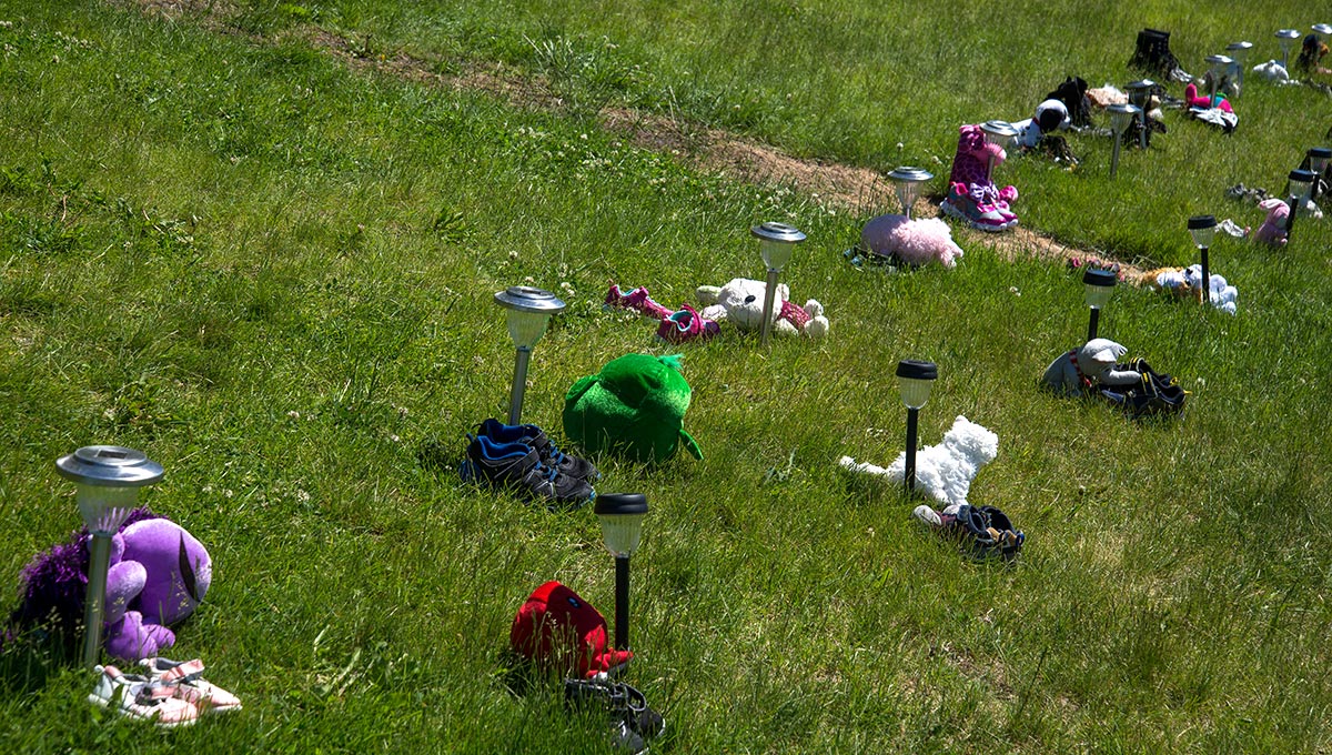 Teddy bears, shoes, and lights are seen on the grass as part of a memorial for victims of the Kamloops Indian Residential Schools