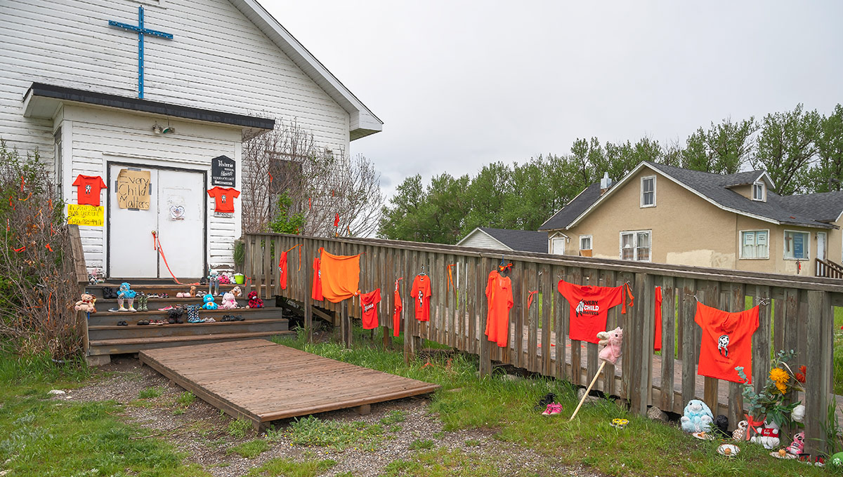 A row of orange t-shirts are hung on a fence outside of a church in the Stoney Nakoda First Nation that mourns the loss of children in residential schools.
