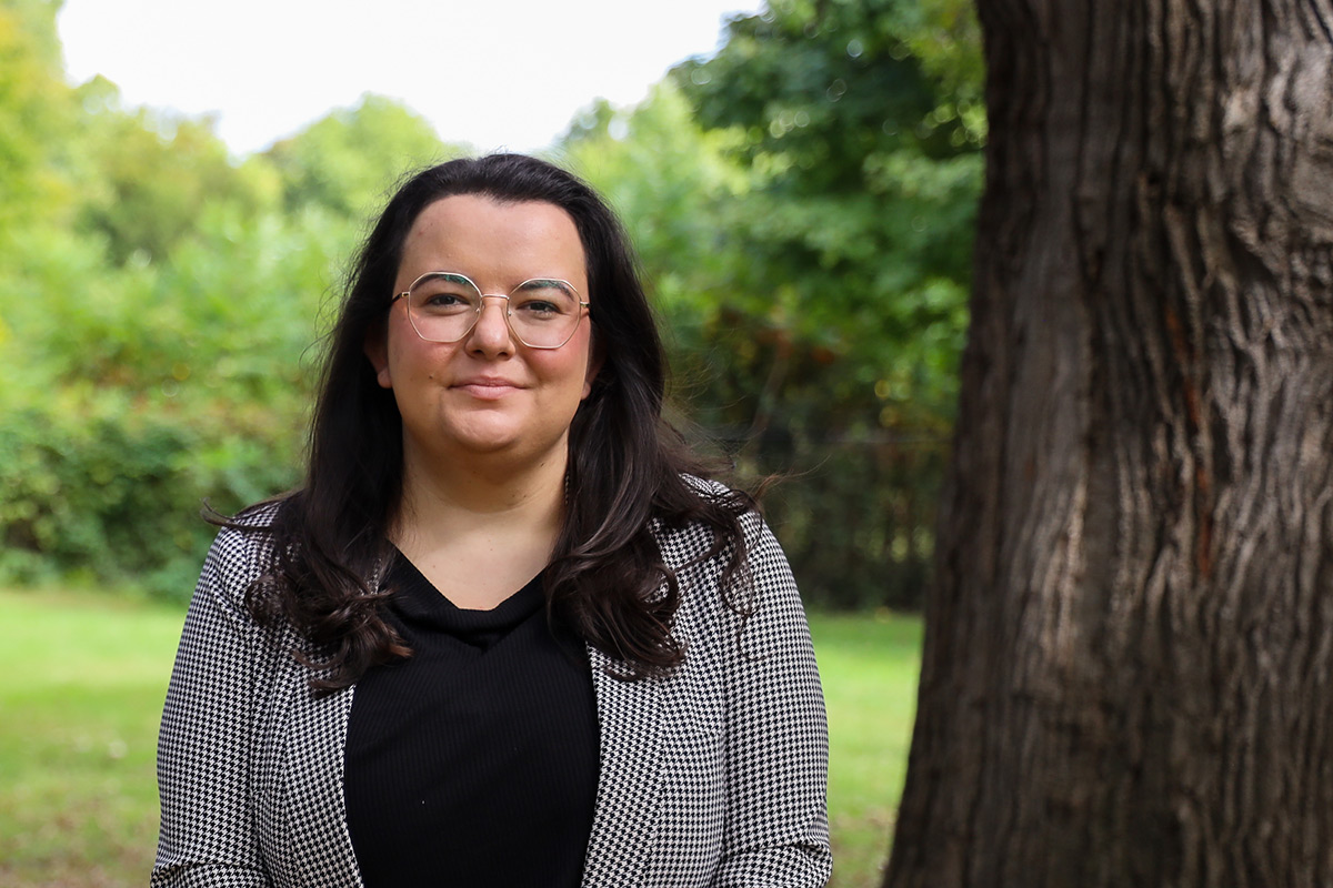 A professional photo of a woman wearing glasses, standing next to a tree.