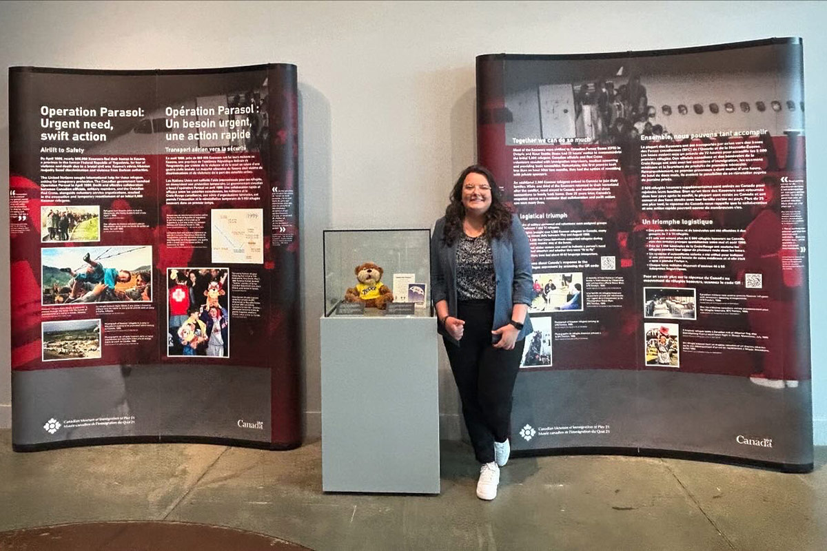 A woman standing cross-legged next to an exhibit.