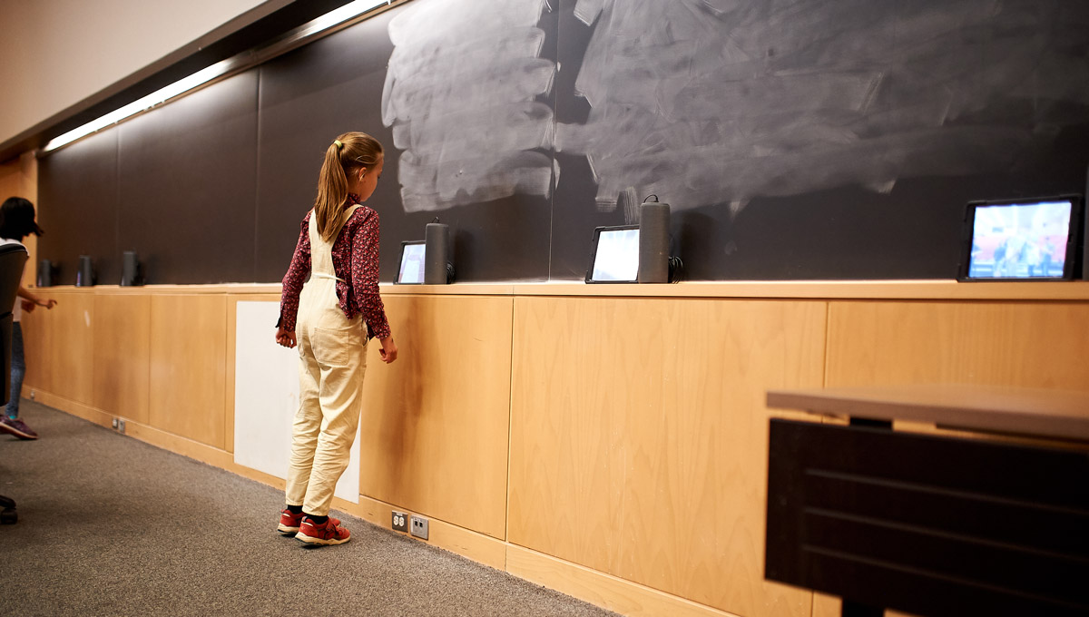 A child interacts with a music-making device positioned on a blackboard.