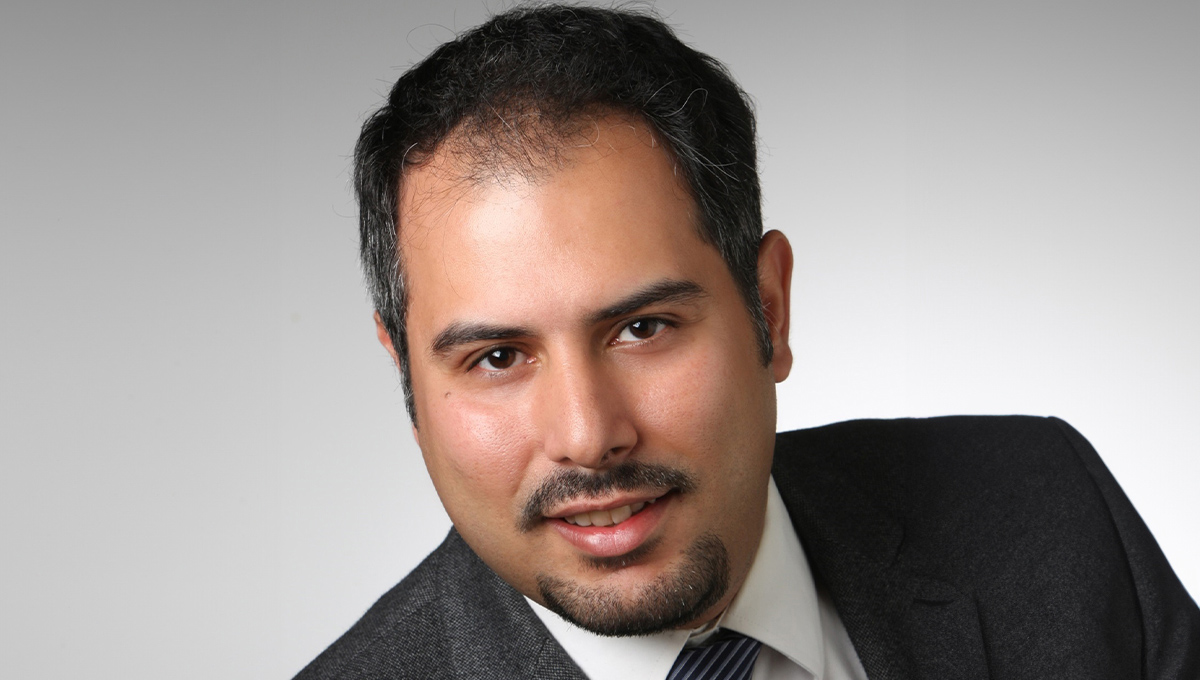 A professional headshot of a man wearing a dark suit.