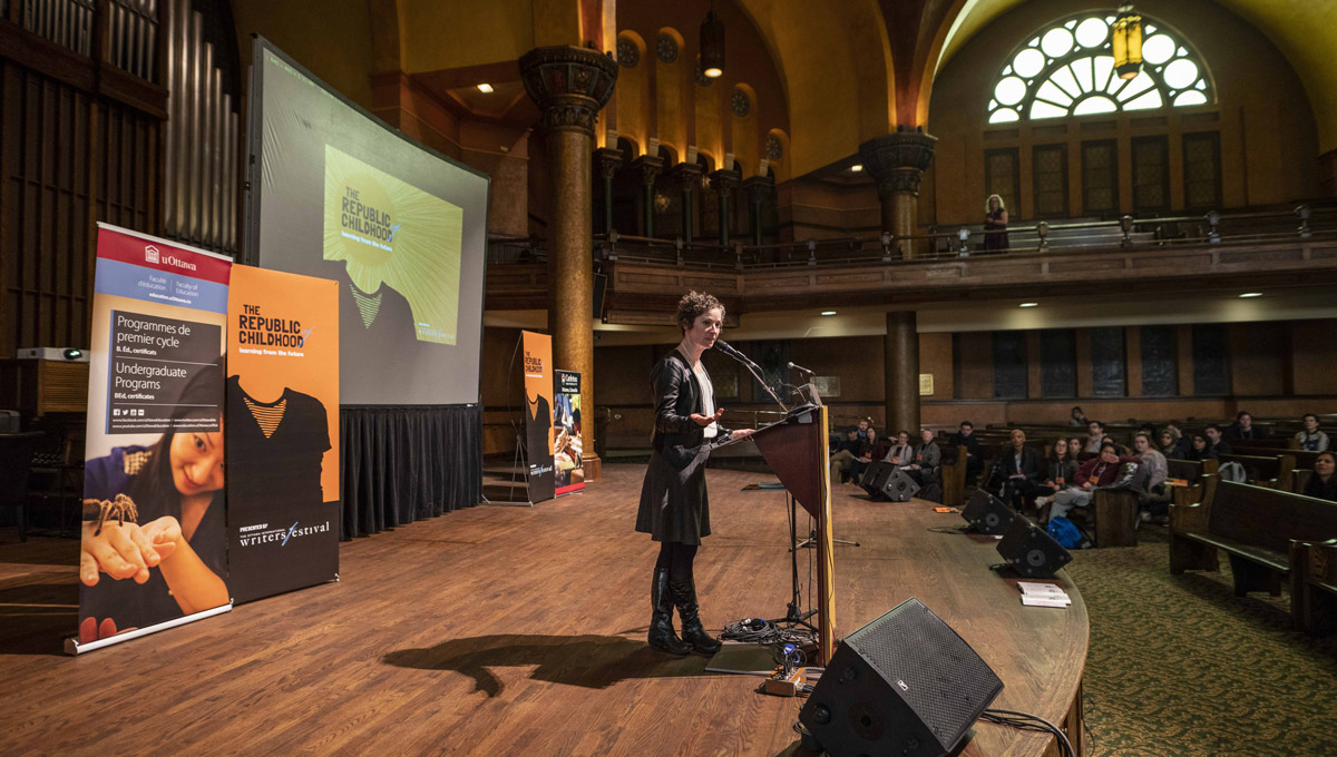 Prof. Jacqueline Kennelly speaks at a podium in the Carleton Dominion-Chalmers Centre.