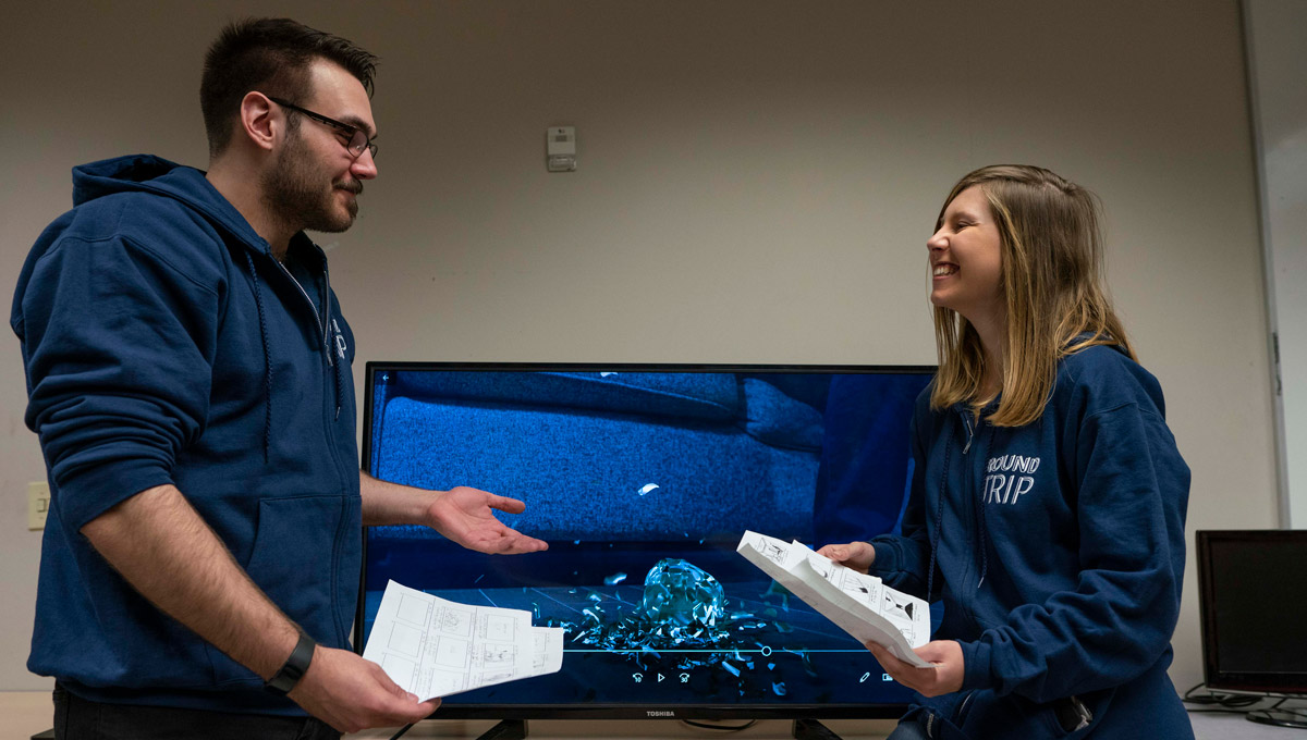 The creators of Round Trip talk in front of a television displaying their work.