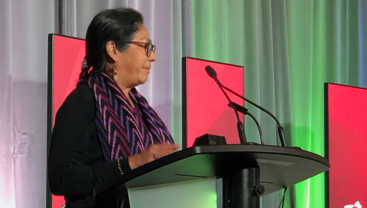 An woman in an Indigenous scarf speaks at the podium during the Royal Society Celebration.