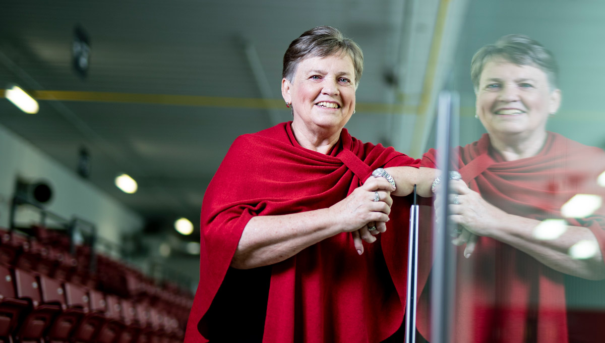 Shirley Mills leans against the glass hockey boards in a rink.