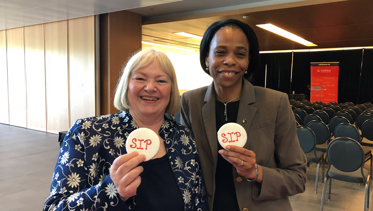 Lorraine Dyke and Patrice Smith hold cookies with "SIP" written on them in decorative frosting.