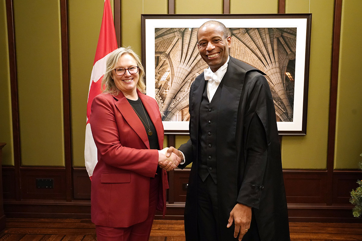 Two people shaking hands with the Canadian flag visible in the background.