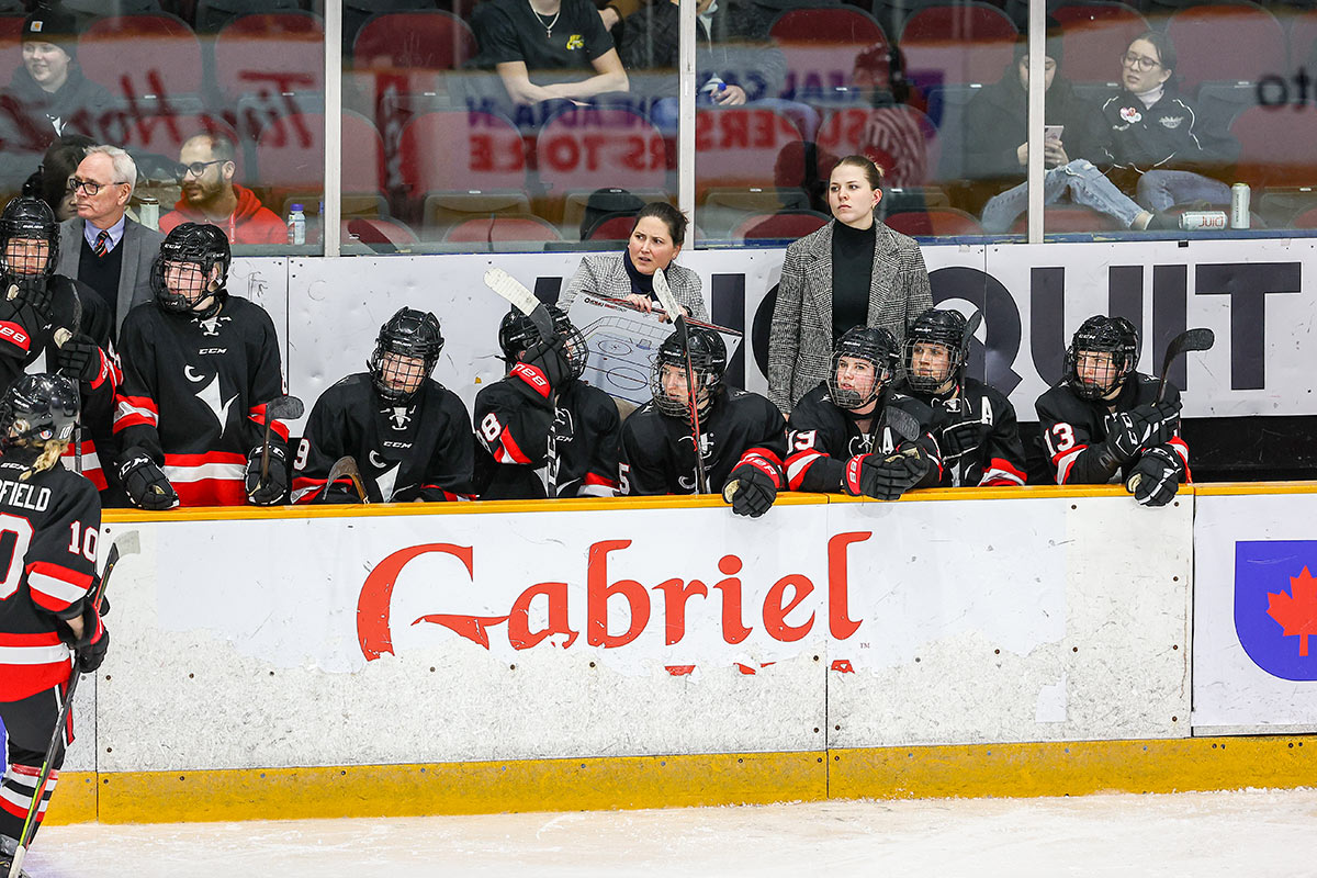 Players and coaches on the bench during a women's hockey game.