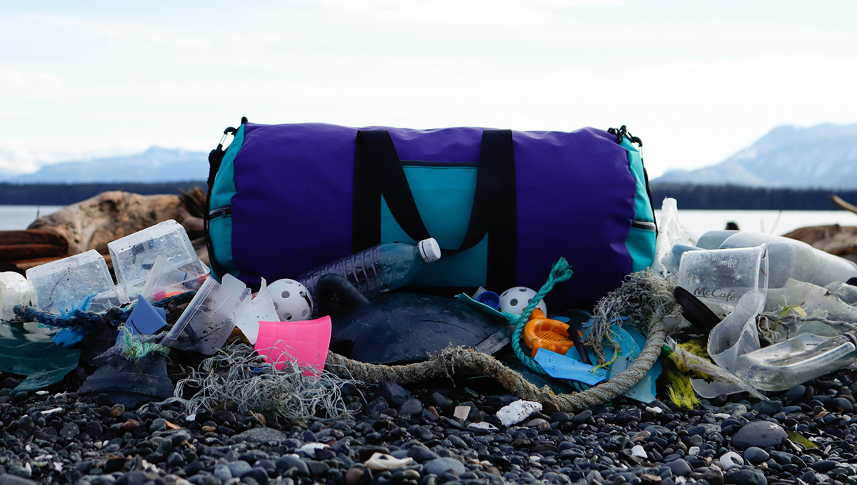 A blue sustainable bag sitting on the beach amongst a pile of garbage