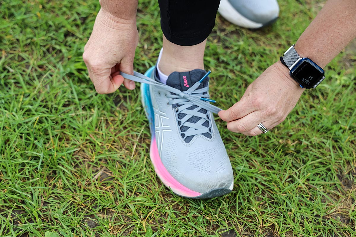 A close up of a shoe being tied by two hands. An Apple Watch can seen on the arm of the person tying the shoe.