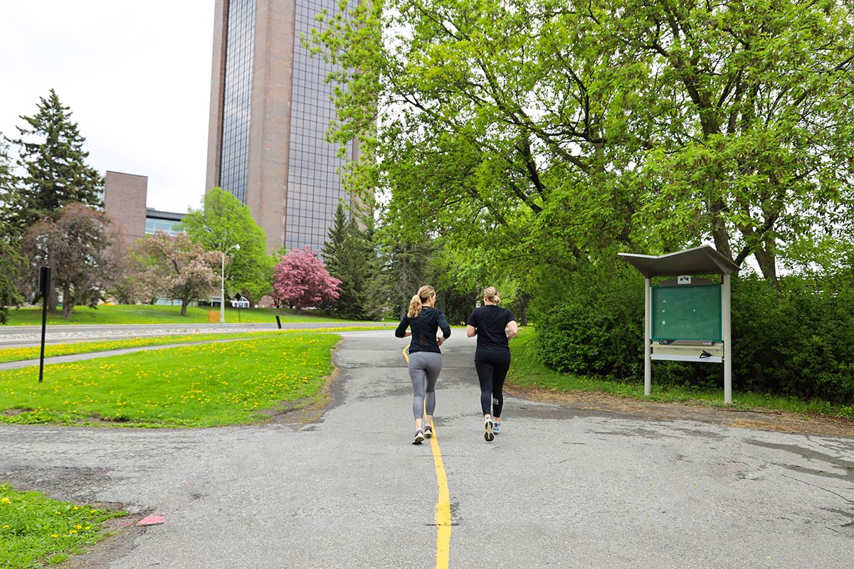 Two runners running away from the camera on a bike path.