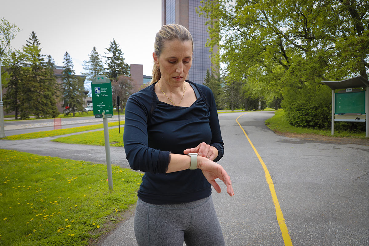 A runner checks a fitness tracker while idling on a path.