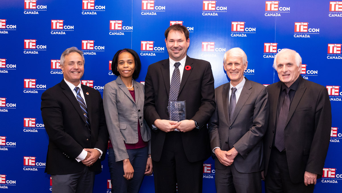 Prof. Steven Muegge poses on stage with Carleton representatives.