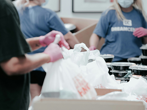 A pair of hands wearing protective gloves holding a grocery bag.