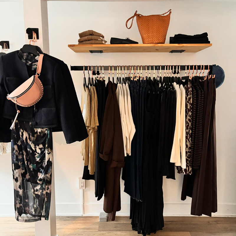 Clothes hanging from a rack, and bags on a shelf above the clothes, as an example of gifting ideas.