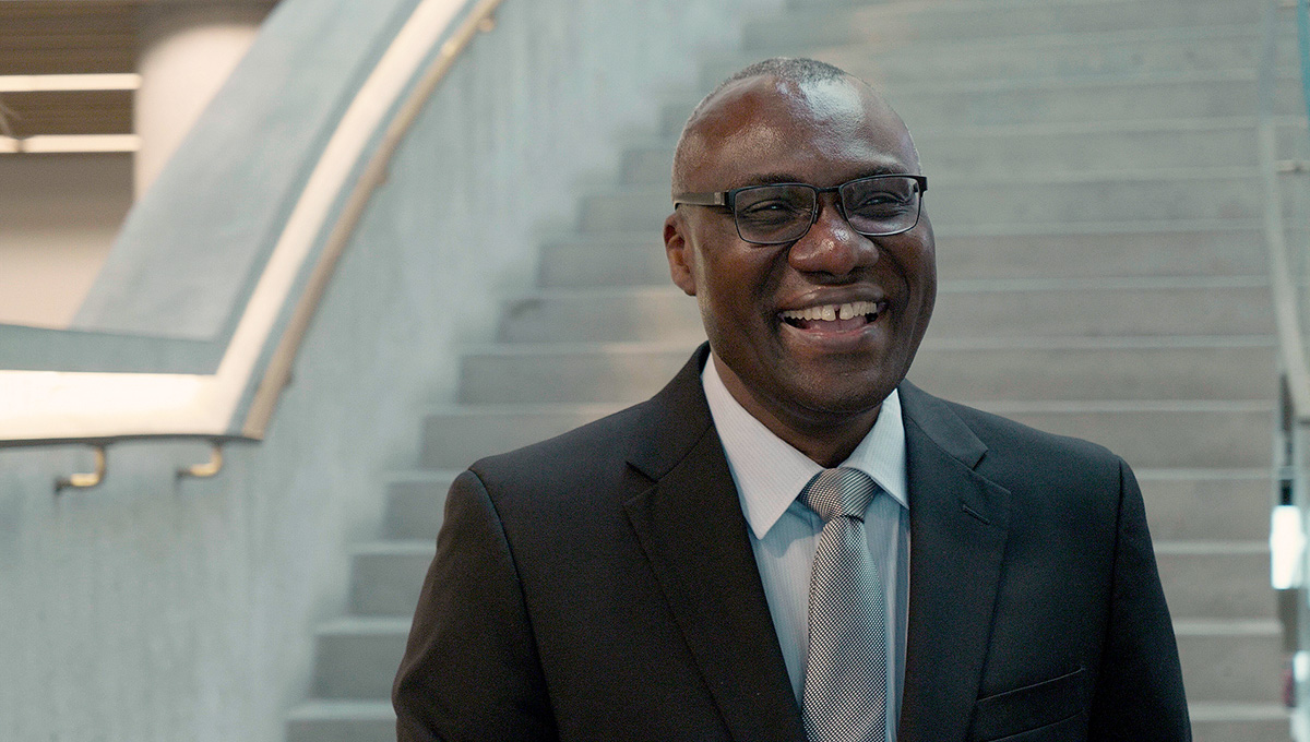 A man wearing glasses and a suit smiles for the camera.