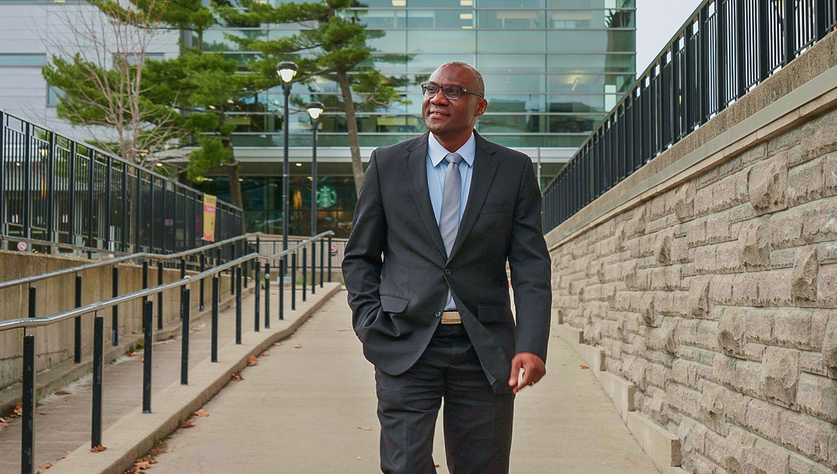 A man in a suit walking down a brick path with one hand in his pocket.