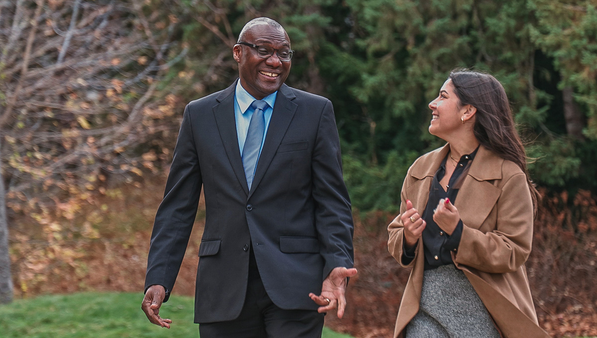 A professionally dressed man and woman share a laugh while walking outside.